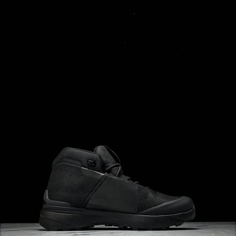 May include: A black high-top boot with a mesh and smooth texture. The boot has a thick sole and a padded collar. The design is sleek and modern, suitable for various outdoor activities. The boot is approximately 7 inches tall.