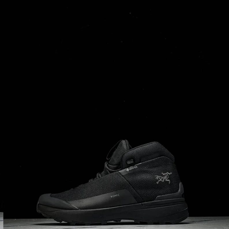 May include: Black hiking boot with a high-top design. The boot features a mesh upper, a thick sole, and the word "KOPIC" printed on the side. A logo of a bird is visible on the side of the boot.
