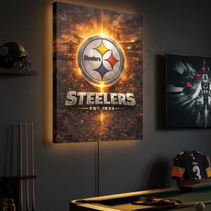 Op de afbeelding: Een verlichte wandkunst met het logo van de Pittsburgh Steelers. Het logo is een zilveren cirkel met een gele, rode en blauwe ster. Het woord "Steelers" staat eronder, met "Est. 1933" eronder. De kunst wordt tentoongesteld in een speelkamer.