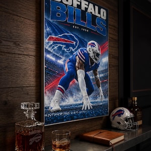Op de afbeelding: Een rechthoekige wandprint met het Buffalo Bills logo en de tekst EST. 1959, waarop een footballspeler in een blauw uniform in een stadion te zien is. De print hangt aan een houten wand boven een plank met een glazen karaf, een glas, een notitieboek en een miniatuurhelm.