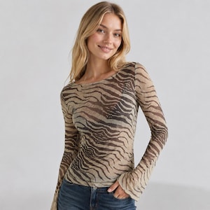 Könnte beinhalten: Ein langärmeliges Oberteil aus einem transparenten, leicht durchscheinenden Stoff mit einem braun-beigen Tigerstreifenmuster. Das Kleidungsstück hat einen weiten, runden Ausschnitt und anliegende Ärmel, die an den Handgelenken leicht ausgestellt sind.