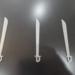 May include: Three identical light gray toy swords arranged in a row. Each sword features a long, straight blade with a slightly curved tip and a simple, D-shaped hand guard at the base of the hilt. The design is flat and uniform in color.
