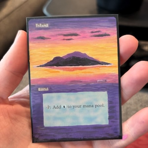 May include: A Magic: The Gathering Island card featuring a sunset over a mountain range. The card has text that reads "Island" at the top and "Land" at the bottom. The card also has text that reads "Add to your mana pool."