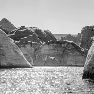 以下が含まれることがあります： 大きな岩石層のある湖の風景の白黒写真。水は太陽光の中で輝き、光を反射しています。岩石層は層状で質感があり、劇的な風景を作り出しています。