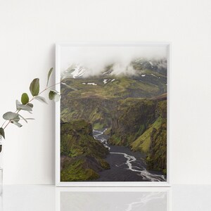 May include: A framed landscape photograph of a canyon with a river winding through it. The canyon walls are green with vegetation, and the riverbed is dark. The top of the canyon is covered in clouds.