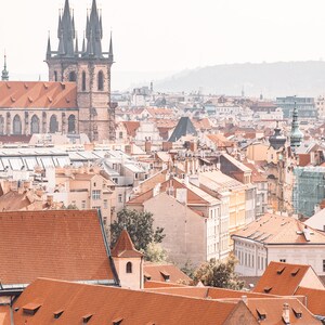 May include: An aerial view of a city with red tiled roofs and a tall church with two spires in the background.