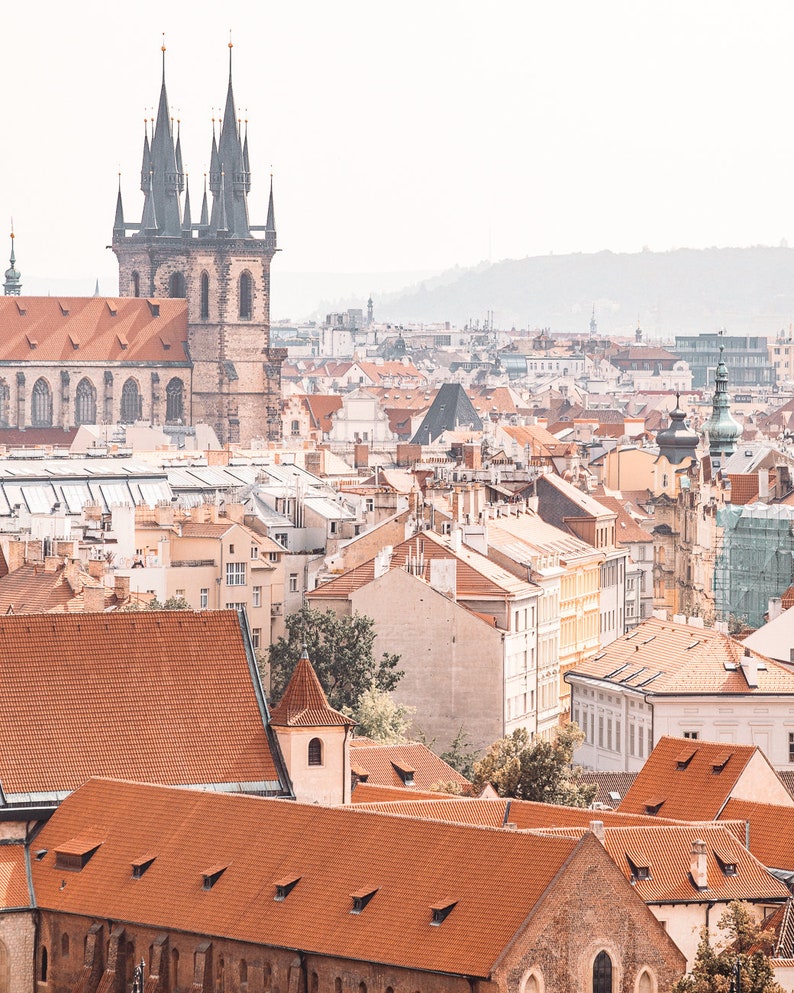 May include: An aerial view of a city with red tiled roofs and a tall church with two spires in the background.