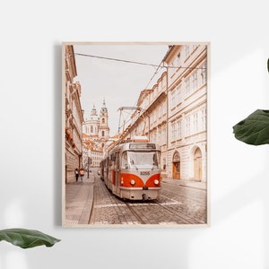 May include: A vintage-style tram travels down a narrow street in Prague, Czech Republic. The street is lined with old buildings and the tram is painted in a red and white color scheme. The tram is numbered 8258.