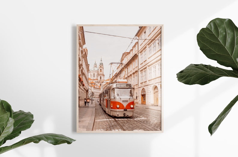 May include: A vintage-style tram travels down a narrow street in Prague, Czech Republic. The street is lined with old buildings and the tram is painted in a red and white color scheme. The tram is numbered 8258.