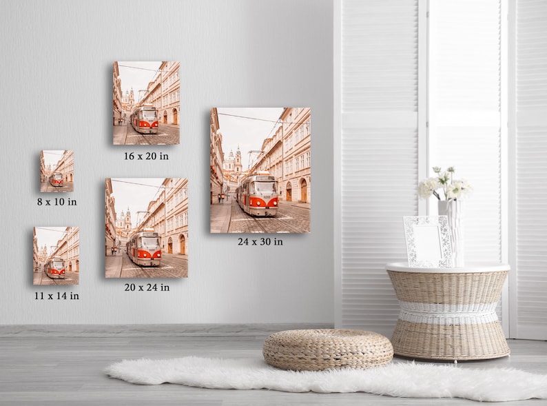 May include: A red and white tram travels down a narrow street lined with buildings in a European city. The street is cobblestone and the buildings are all beige with white trim. The tram is in focus and the buildings are slightly out of focus. The image is a photograph.