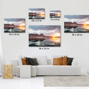 May include: Canvas prints of a sunset over a lake, with sizes ranging from 30.5 x 20.3 cm to 91.4 x 61 cm. The artwork depicts a landscape with a vibrant sunset, water reflections, and a cloudy sky. The prints are displayed on a white wall above a white sofa.
