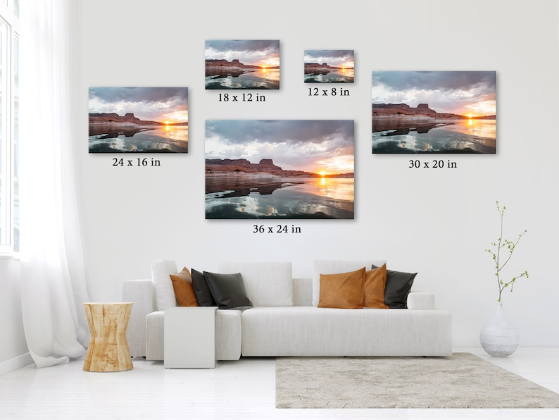 May include: Canvas prints of a sunset over a lake, with sizes ranging from 30.5 x 20.3 cm to 91.4 x 61 cm. The artwork depicts a landscape with a vibrant sunset, water reflections, and a cloudy sky. The prints are displayed on a white wall above a white sofa.