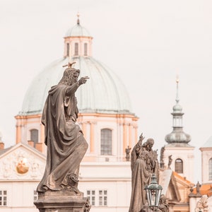 May include: A close-up of a statue of a man pointing towards a large, domed building. The statue is made of stone and is weathered. The building is in the background and is a light beige color with a green dome.
