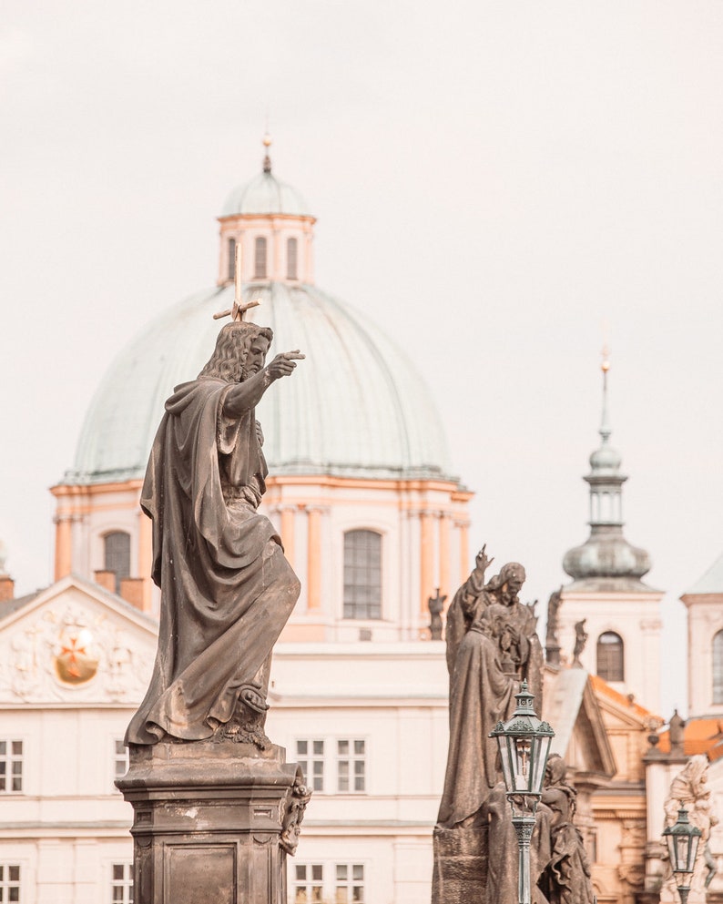 May include: A close-up of a statue of a man pointing towards a large, domed building. The statue is made of stone and is weathered. The building is in the background and is a light beige color with a green dome.