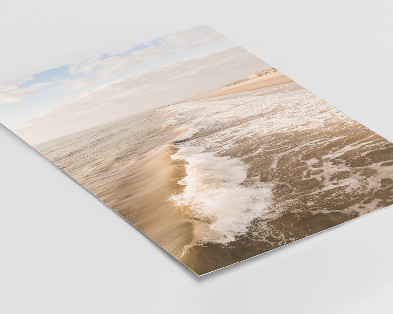 Pu&ograve; includere: Fotografia di una scena di spiaggia con vista prospettica. L'immagine cattura le onde dell'oceano mentre si muovono verso la riva. L'acqua &egrave; un mix di marrone e bianco, con il cielo azzurro pallido e beige.