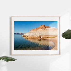May include: A framed landscape photograph showing a lake and a rock formation under a clear blue sky. The rock formation has layers of white and brown hues. The water reflects the sky and the rock formation.