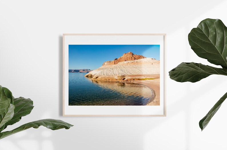 May include: A framed landscape photograph showing a lake and a rock formation under a clear blue sky. The rock formation has layers of white and brown hues. The water reflects the sky and the rock formation.