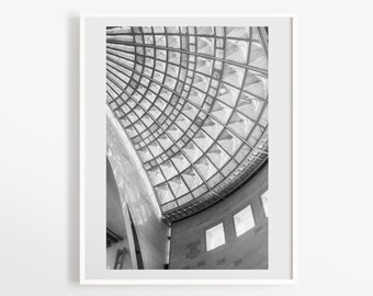 May include: Black and white architectural print featuring a curved glass ceiling with a geometric grid pattern. The image captures a section of a building's interior, showcasing the interplay of light and shadow. The print is framed in a white border.