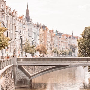 May include: A view of a bridge over a river in Prague, Czech Republic. The bridge is made of concrete and has a stone arch. The river is brown and the water is calm. The buildings on the other side of the river are tall and have colorful facades.
