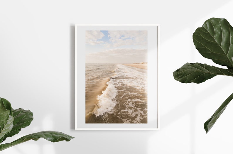 Pu&ograve; includere: Una stampa incorniciata con una serena scena di spiaggia. La fotografia cattura le onde dell'oceano che si infrangono sulla riva sotto un cielo nuvoloso. La tavolozza dei colori &egrave; morbida, con toni caldi di beige e blu, creando un'estetica rilassante.