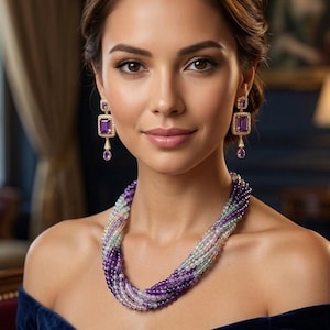 Peut inclure: Une femme porte un collier à plusieurs rangs et des boucles d'oreilles assorties. Le collier est composé de perles violettes, blanches et vertes. Les boucles d'oreilles présentent une pierre violette rectangulaire et une pierre plus petite en forme de goutte. Elle porte une robe bleu foncé.