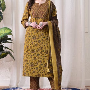 May include: A mustard yellow kurta featuring a dark brown floral print, a notched neckline, and three-quarter sleeves. It is paired with matching dark brown floral print trousers and a long, dark brown floral print dupatta with a mustard yellow border.