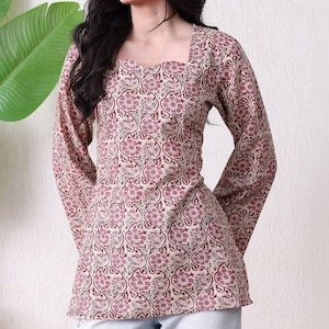Puede incluir: Una blusa de manga larga con escote cuadrado y un patrón floral repetitivo en color granate y crema. La prenda tiene un corpiño ajustado que se ensancha ligeramente en la cintura, con mangas largas y un estampado botánico detallado.