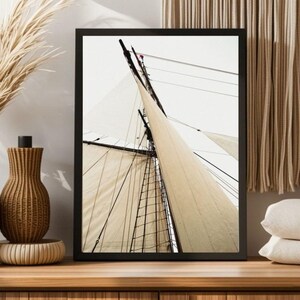 Peut inclure: Une impression d'art encadrée montrant une vue en contre-plongée du mât et du gréement d'un voilier sur un ciel clair. L'image présente de grandes voiles en toile blanc cassé tendues, des mâts en bois sombre et un réseau complexe de cordages noirs.