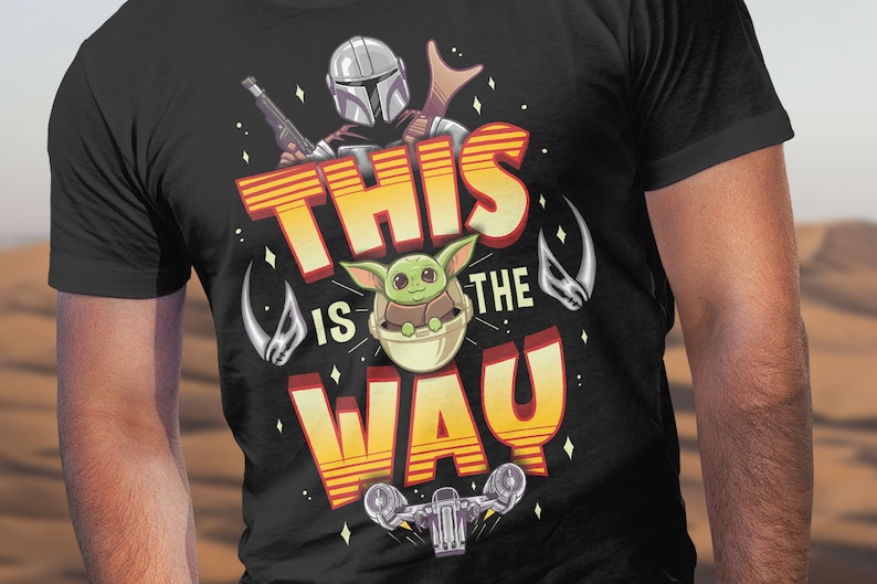 Może przedstawiać: Czarny T-shirt z ż&oacute;łto-pomarańczową grafiką przedstawiającą postać Mandalorianina i małego Yody. Grafika zawiera napis "This is the Way".