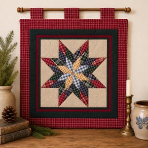 Puede incluir: Un tapiz de tela cuadrado que presenta un bloque de edredón central con forma de estrella de ocho puntas hecho de tela a cuadros roja, azul, verde y amarilla. La estrella está sobre un fondo beige con bordes negros y rojos, colgado de una vara.
