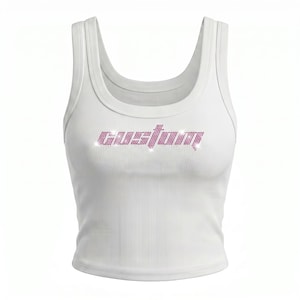 Puede incluir: Una camiseta de tirantes blanca acanalada con la palabra custom escrita en pedrería rosa en el pecho. La prenda tiene un escote redondo y tirantes anchos, con el texto rosa brillante creando un contraste marcado sobre la tela blanca.