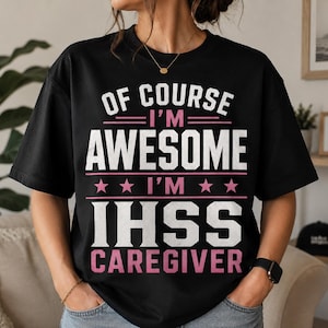 May include: A black short-sleeved t-shirt featuring white and pink text that reads: OF COURSE I'M AWESOME I'M IHSS CAREGIVER. The design includes horizontal lines and two pink stars separating the text lines, printed on the front of the garment.