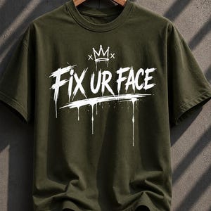 Könnte beinhalten: Olivgrünes T-Shirt mit dem weißen Schriftzug "FIX UR FACE" in einem Graffiti-Stil, mit einer Kronengrafik. Das Design beinhaltet tropfende Farbeffekte.