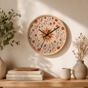 Pode incluir: Relógio de parede redondo com moldura de madeira clara. O mostrador apresenta um design de raio de sol em laranja e amarelo, rodeado por elementos florais e botânicos. Os ponteiros pretos indicam as horas. Um elemento decorativo para casa.