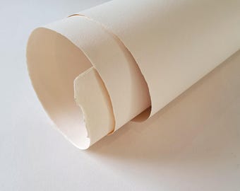 May include: A single sheet of off-white, cream-colored paper rolled into a cylindrical shape. The paper features a distinct, uneven, and textured deckled edge at the opening of the roll, showcasing a fibrous and heavy-weight appearance.