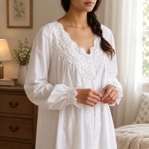 May include: A long-sleeved white nightgown featuring a V-neckline adorned with intricate white lace detailing. The garment includes gathered fabric at the shoulders, ruffled cuffs at the wrists, and a vertical lace trim running down the front center.