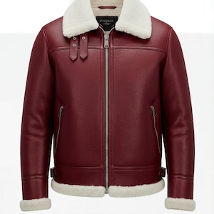 Peut inclure: Veste en cuir bordeaux avec col et doublure en peau de mouton blanche. La veste est dotée d'une fermeture éclair, de deux poches latérales et de boucles. La marque "MAVERICK HERITAGE" est visible.