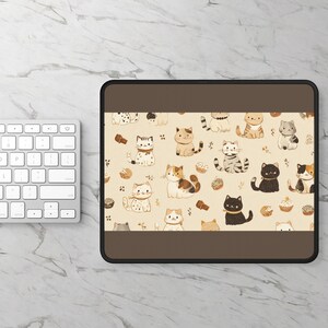 May include: A rectangular mouse mat with a brown border and a beige centre. It features a repeating pattern of cartoon cats and cupcakes. The cats are in various poses and colours, including black, orange, and grey.