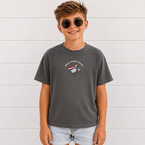 K&ouml;nnte beinhalten: Ein anthrazitfarbenes Kurzarm-T-Shirt mit einer Grafik einer wei&szlig;en Gans, die ein Cape in den Farben der kroatischen Flagge tr&auml;gt und einen Fu&szlig;ball kickt. Der Text "Off to watch Croatia" ist in einem wei&szlig;en Bogen &uuml;ber der Gans gedruckt.