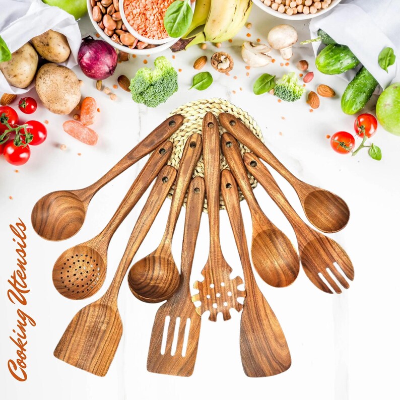 May include: A collection of wooden cooking utensils, including spoons, spatulas, and a pasta fork, arranged on a white surface. The utensils are made of a light brown wood and are surrounded by fresh vegetables and grains. The text "Cooking Utensils" is visible.