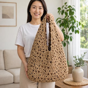 Könnte beinhalten: Eine hellbraune Häkeltasche mit Blumenmuster. Die Tasche wird von einer Person hochgehalten. Die Tasche besteht aus hellbraunem Garn und hat eine große Öffnung. Die Tasche ist hellbraun.
