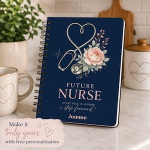 May include: A dark blue spiral-bound notebook featuring a silver stethoscope shaped like a heart, a pink flower, and the text "FUTURE NURSE EVERY PAGE IS ANOTHER step forward" with the name "Joanne" printed in white and pink lettering.
