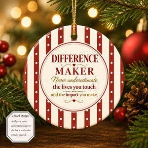 May include: A round ceramic Christmas ornament featuring a cream background with vertical red stripes and white dots. The center text reads: DIFFERENCE MAKER, Never underestimate the lives you touch and the impact you make. It hangs from a gold cord.