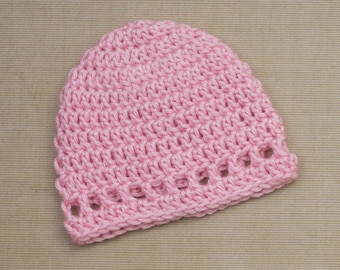 May include: A light pink crocheted beanie hat. The hat is made of a soft yarn and features a textured stitch pattern. The brim has a decorative openwork design. This handmade hat is suitable for babies and children.