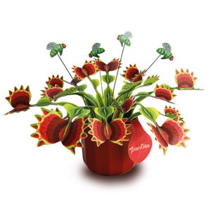 May include: A paper Venus flytrap plant in a red pot with green and red serrated leaves and four green flies on thin black wires. A red tag attached to the pot features the white text plantlike. The plant has multiple open traps.