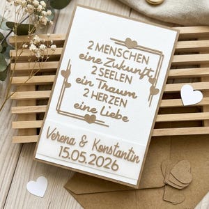 May include: A handmade wedding card with the text "2 people, a future, 2 souls, a dream, 2 hearts, one love." The card includes the names "Verena & Konstantin" and the date "15.05.2026". The card is white with brown accents and a brown envelope.