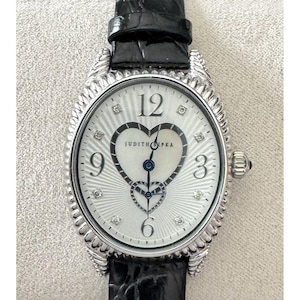Puede incluir: Reloj ovalado plateado con esfera blanca con diseño de corazón y la marca "JUDITH RIPKA". El reloj tiene una correa de cuero negro y pequeños detalles de diamantes. La esfera muestra los números 12, 3, 6 y 9.