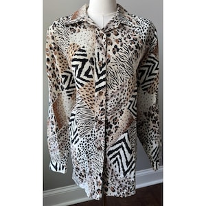 Può includere: Camicia button-down con un design a stampa animalier misto. La camicia presenta un collage di motivi, tra cui macchie di leopardo, strisce zebrate e forme geometriche nelle tonalità del marrone, nero e crema. La camicia a maniche lunghe è esposta su un manichino.