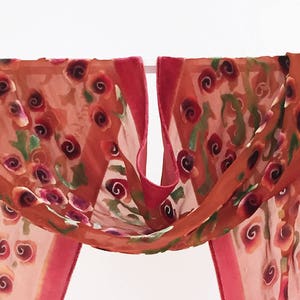 May include: A sheer pink scarf with a floral pattern of orange and green roses. The scarf is made of a lightweight fabric and has a delicate, feminine feel.