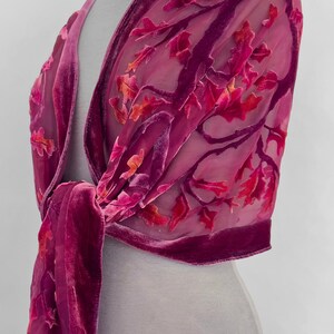 May include: A pink velvet shawl with a floral design. The shawl is draped over a mannequin and tied at the neck.